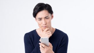 スマートフォンを見ながら悩む男性